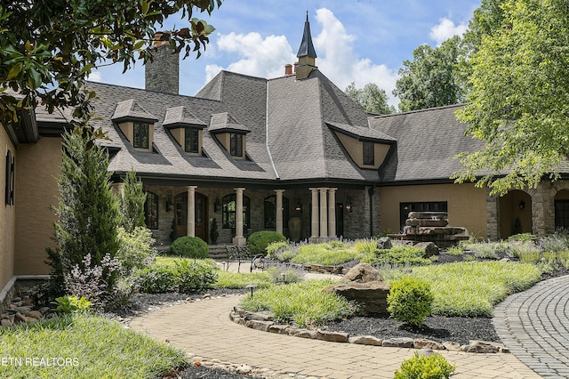 view of front of house featuring stone siding, a shingled roof, a chimney, and stucco siding