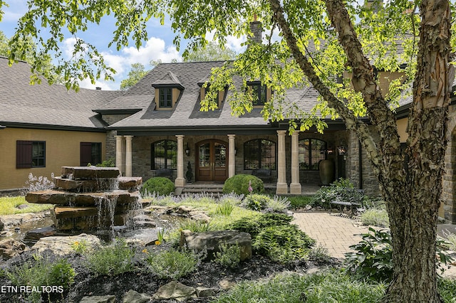 view of front of home with french doors, stucco siding, a shingled roof, covered porch, and stone siding