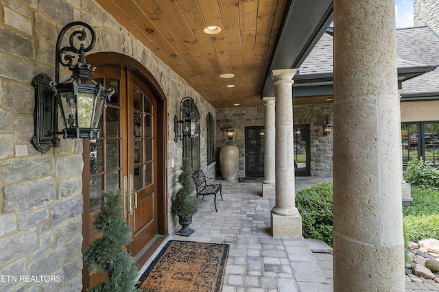 doorway to property with stone siding, french doors, and roof with shingles