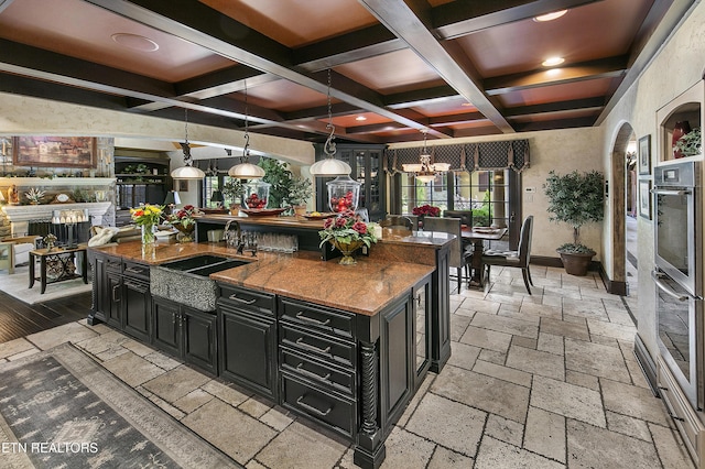 kitchen featuring coffered ceiling, a sink, stone tile flooring, and dark cabinets