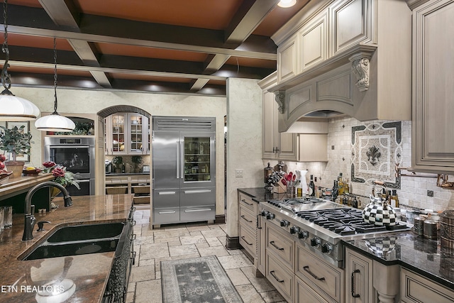 kitchen with stone tile floors, glass insert cabinets, appliances with stainless steel finishes, cream cabinets, and a sink