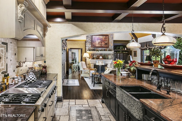 kitchen with dark cabinets, beamed ceiling, stainless steel gas stovetop, a fireplace, and a sink