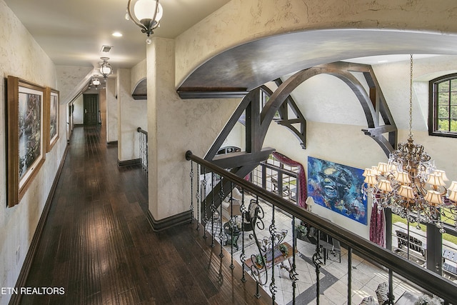 hall featuring a chandelier, wood-type flooring, visible vents, and a textured wall