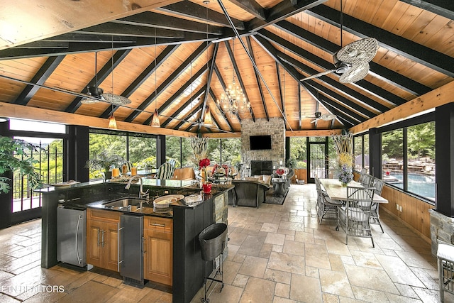 unfurnished sunroom featuring lofted ceiling with beams, a stone fireplace, a sink, wood ceiling, and a ceiling fan