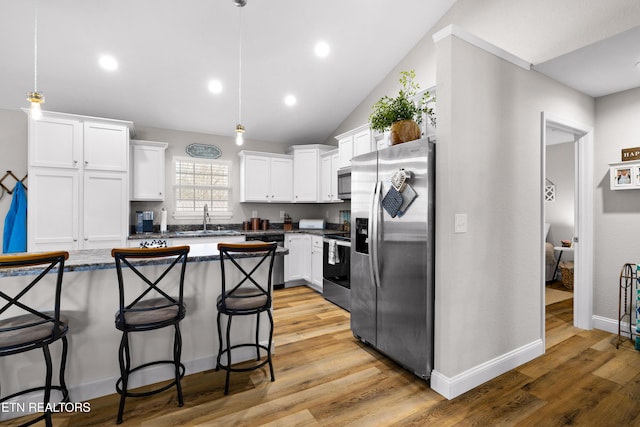 kitchen featuring white cabinets, a breakfast bar area, stainless steel appliances, light wood-type flooring, and a sink