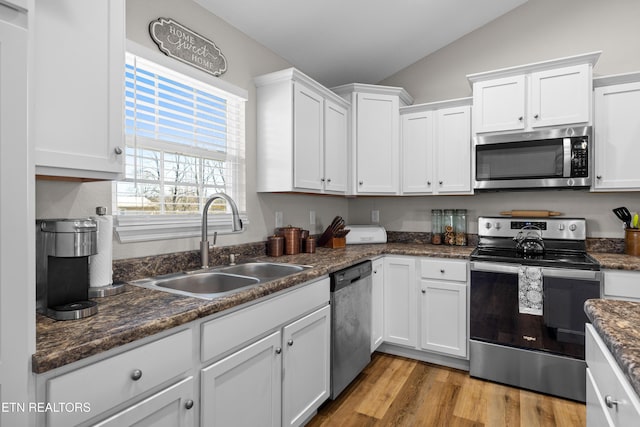 kitchen featuring stainless steel appliances, a sink, white cabinets, vaulted ceiling, and light wood-type flooring