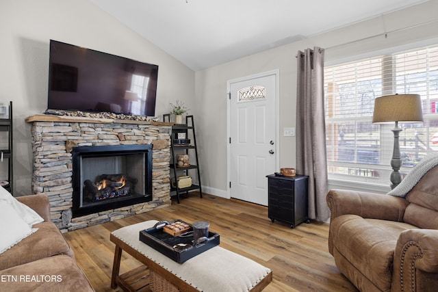 living room featuring lofted ceiling, a stone fireplace, wood finished floors, and baseboards