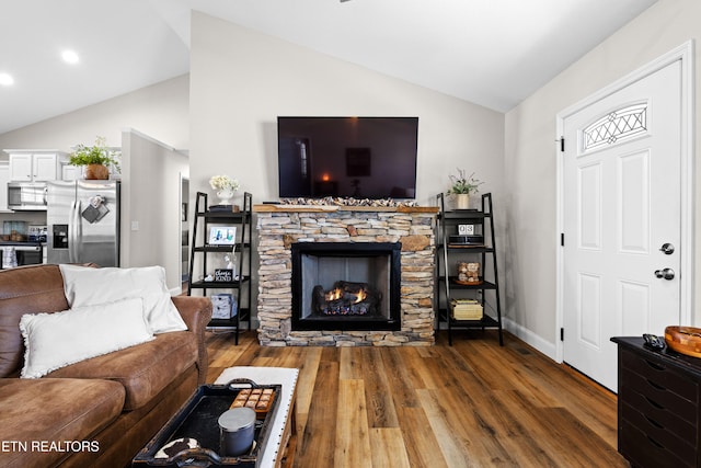 living area featuring vaulted ceiling, a stone fireplace, wood finished floors, and baseboards