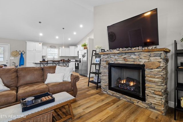 living room with high vaulted ceiling, a stone fireplace, recessed lighting, and light wood-style floors