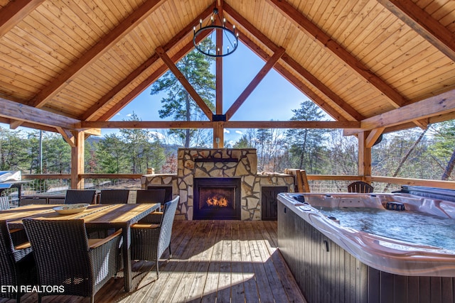 wooden terrace with a hot tub, an outdoor stone fireplace, and outdoor dining area