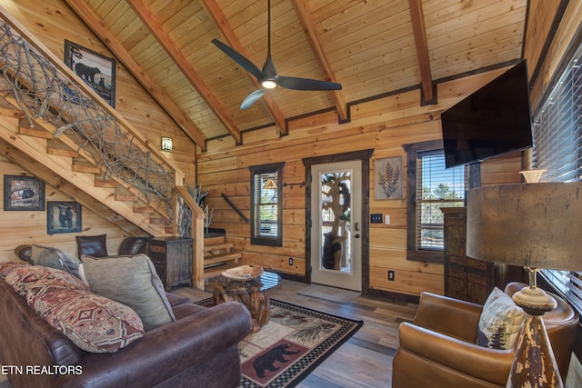 living area featuring beam ceiling, wooden walls, wood finished floors, wooden ceiling, and stairs