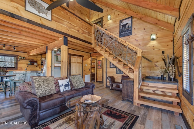 living room featuring beam ceiling, stairway, wood walls, ceiling fan, and hardwood / wood-style floors