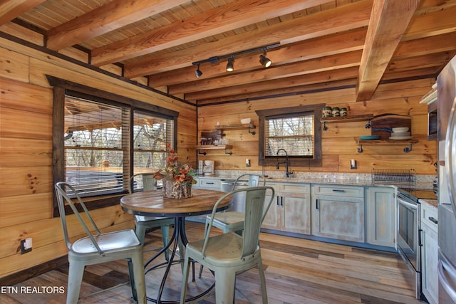 dining room with light wood finished floors, wooden walls, and beamed ceiling