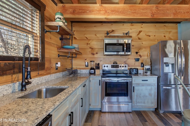 kitchen featuring wooden walls, appliances with stainless steel finishes, wood finished floors, open shelves, and a sink