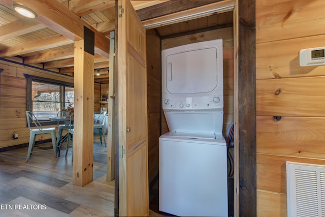 laundry area featuring stacked washer and clothes dryer, wood ceiling, wood walls, wood finished floors, and laundry area