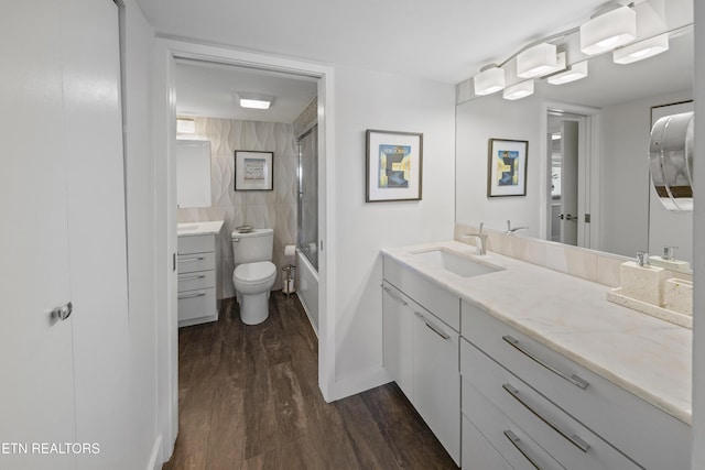 bathroom with toilet, shower / bath combination with glass door, wood finished floors, vanity, and tile walls