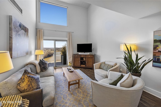 living room with dark wood-type flooring, a towering ceiling, and baseboards