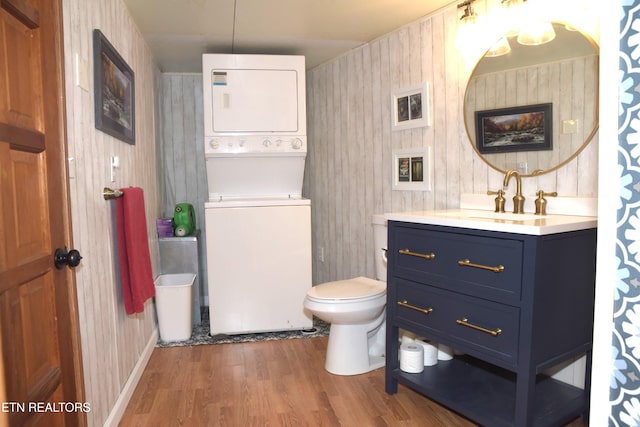 bathroom with stacked washer and clothes dryer, vanity, toilet, and wood finished floors