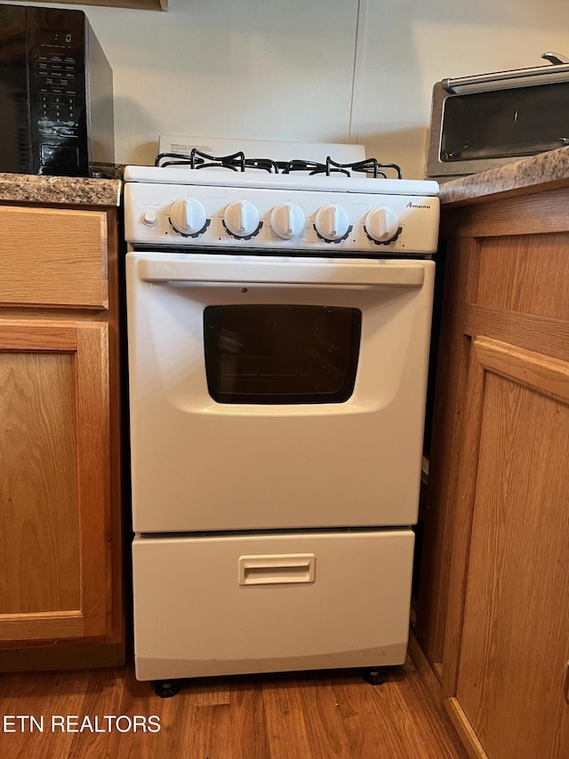 kitchen with a toaster, white range with gas stovetop, and wood finished floors