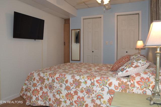 bedroom featuring a paneled ceiling, ceiling fan, and two closets