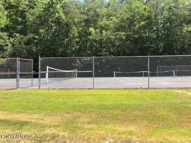 view of community featuring a tennis court, a yard, and fence