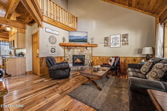 living room featuring wooden ceiling, a wainscoted wall, a stone fireplace, and hardwood / wood-style flooring