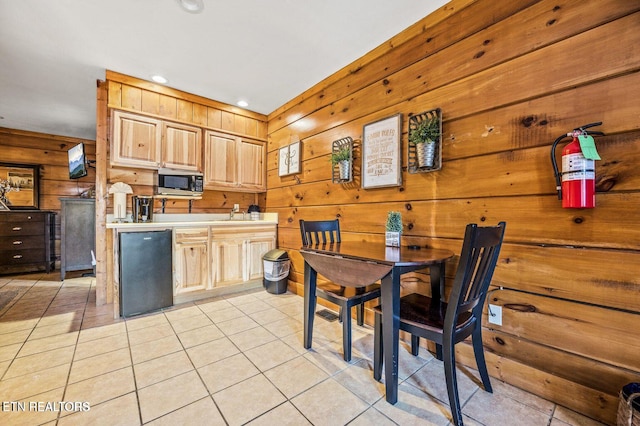 kitchen with refrigerator, light tile patterned floors, stainless steel microwave, light brown cabinetry, and wood walls