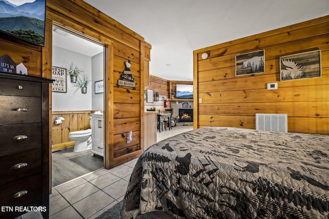 bedroom with tile patterned flooring, wooden walls, a wainscoted wall, visible vents, and a lit fireplace