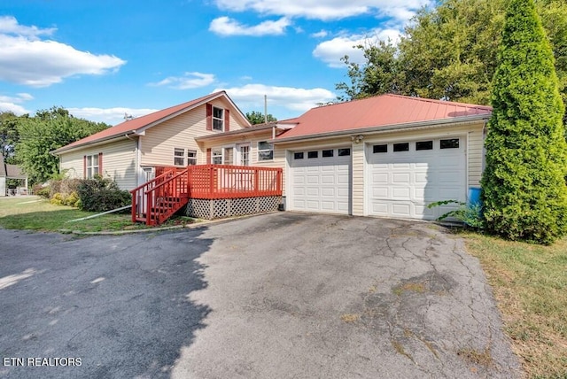 ranch-style home with a garage, metal roof, a deck, and aphalt driveway