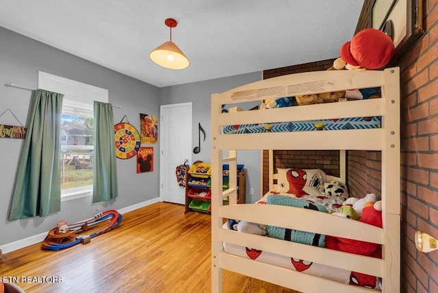 bedroom featuring brick wall, baseboards, and wood finished floors