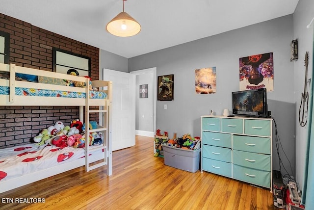 bedroom featuring light wood finished floors and brick wall