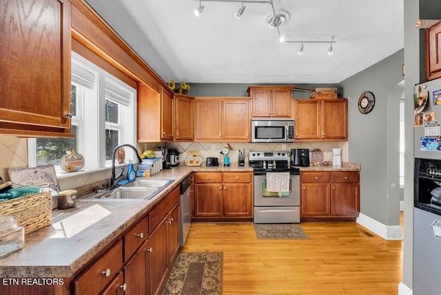 kitchen featuring arched walkways, stainless steel appliances, backsplash, light wood-style flooring, and a sink