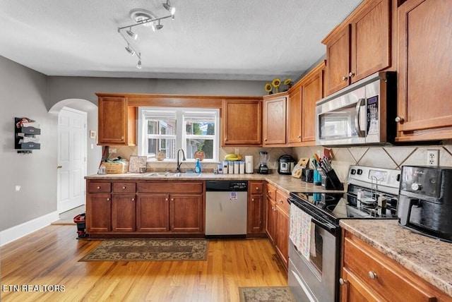 kitchen featuring light wood finished floors, arched walkways, appliances with stainless steel finishes, a sink, and backsplash