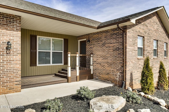 doorway to property with brick siding and roof with shingles