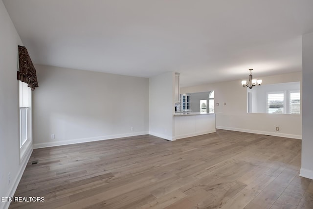 unfurnished living room with a notable chandelier, wood finished floors, visible vents, and baseboards