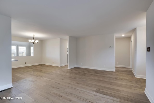 empty room with a notable chandelier, wood finished floors, visible vents, and baseboards