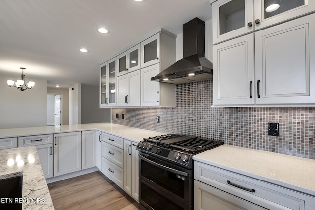 kitchen with backsplash, double oven range, white cabinetry, and wall chimney range hood