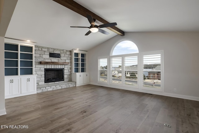 unfurnished living room featuring beam ceiling, wood finished floors, a fireplace, baseboards, and ceiling fan