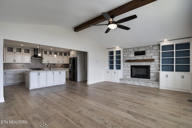 kitchen with beam ceiling, wall chimney range hood, open floor plan, freestanding refrigerator, and light wood finished floors