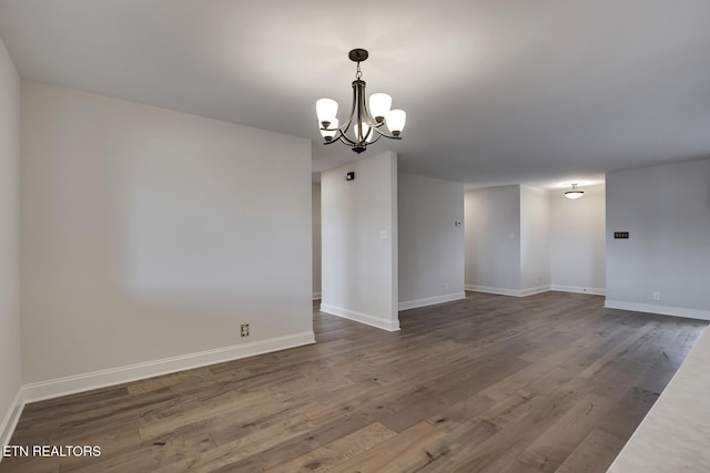 unfurnished room with baseboards, a notable chandelier, and wood finished floors