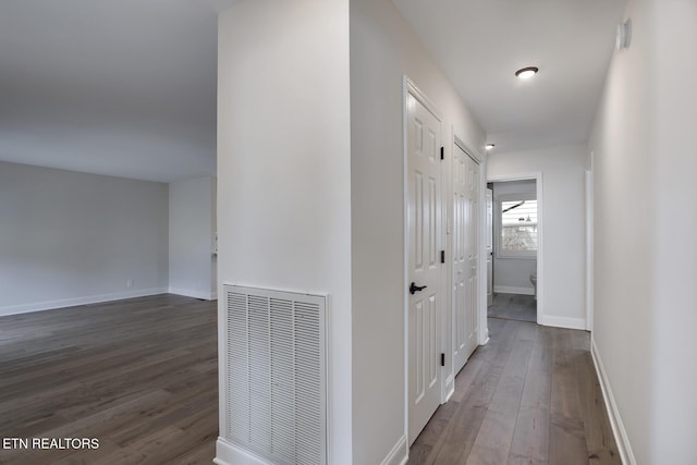 corridor featuring visible vents, baseboards, and dark wood-style floors