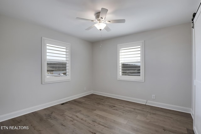 empty room featuring plenty of natural light, ceiling fan, a barn door, and wood finished floors