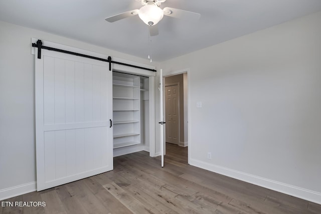 unfurnished bedroom with baseboards, a ceiling fan, a barn door, and wood finished floors