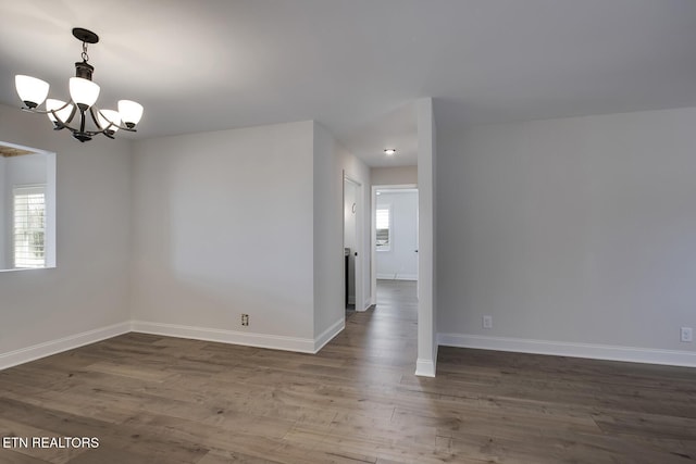 spare room featuring baseboards, an inviting chandelier, and wood finished floors