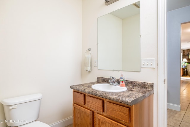 half bath with toilet, tile patterned floors, baseboards, and vanity