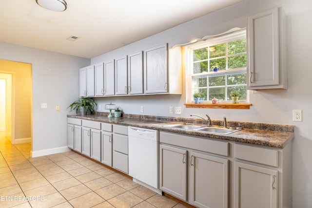 kitchen with dark countertops, white dishwasher, a sink, and baseboards