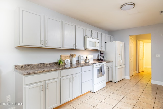 kitchen featuring light tile patterned floors, white appliances, dark countertops, and baseboards