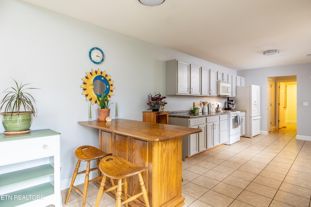 kitchen featuring white appliances, baseboards, a peninsula, a kitchen bar, and light tile patterned flooring