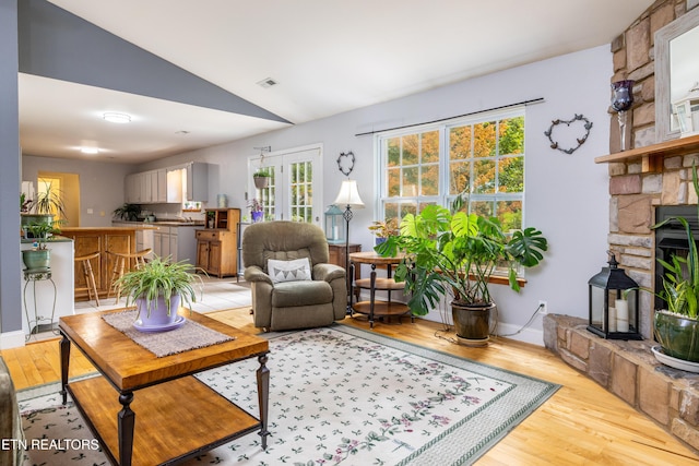 living room featuring vaulted ceiling, a stone fireplace, light wood-type flooring, and visible vents