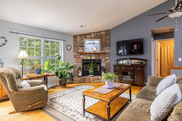 living area with visible vents, a ceiling fan, lofted ceiling, wood finished floors, and a stone fireplace